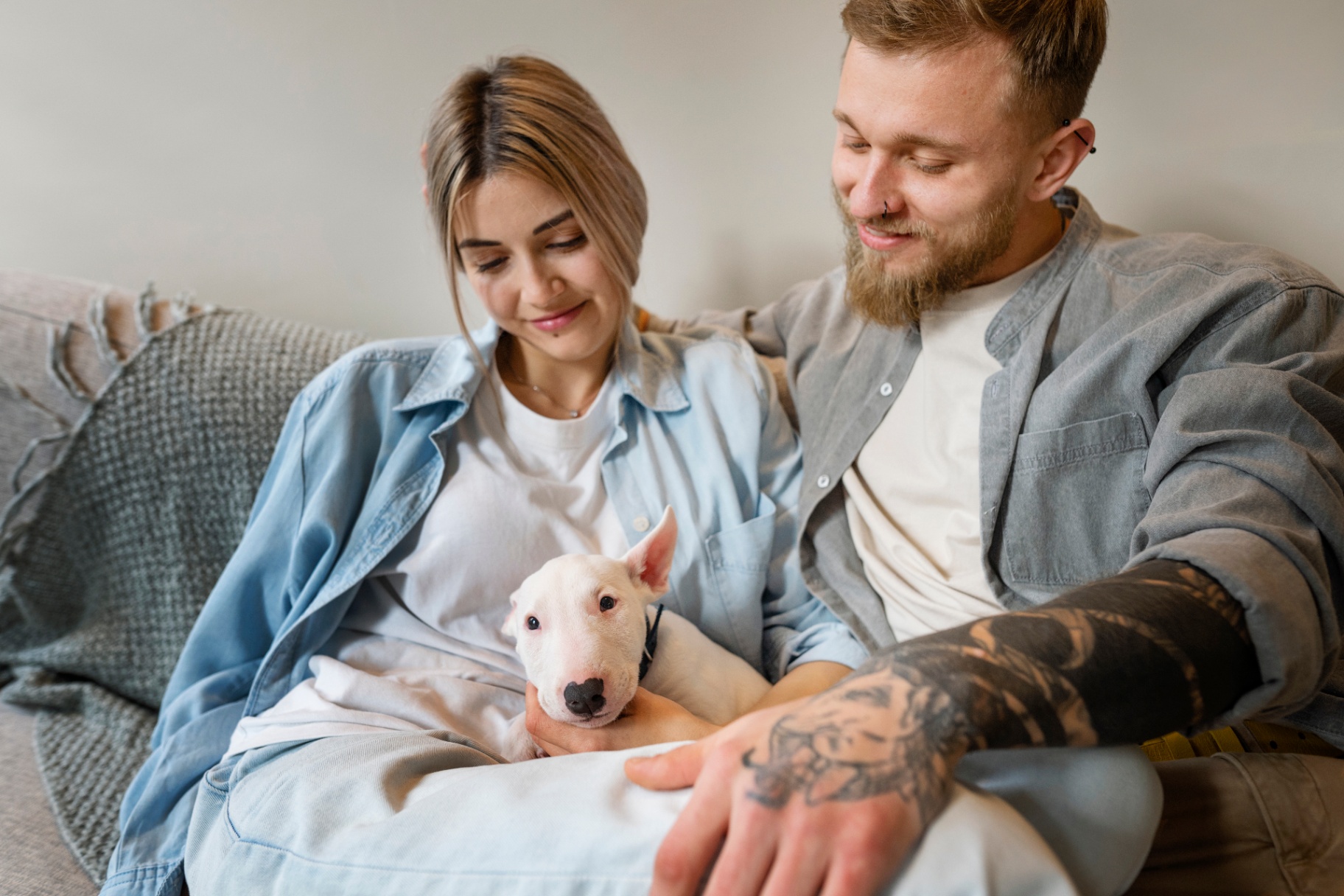 A young couple on a couch with their white bull terrier puppy